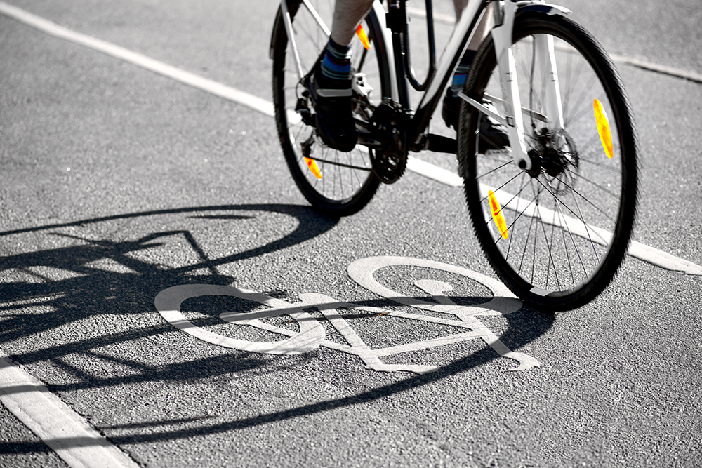 Un cycliste fait ombre sur un symbole 'vélo' sur une piste cyclable